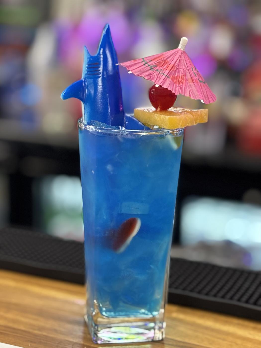 A tall blue cocktail at our bar, with a paper umbrella, cherry and pineapple