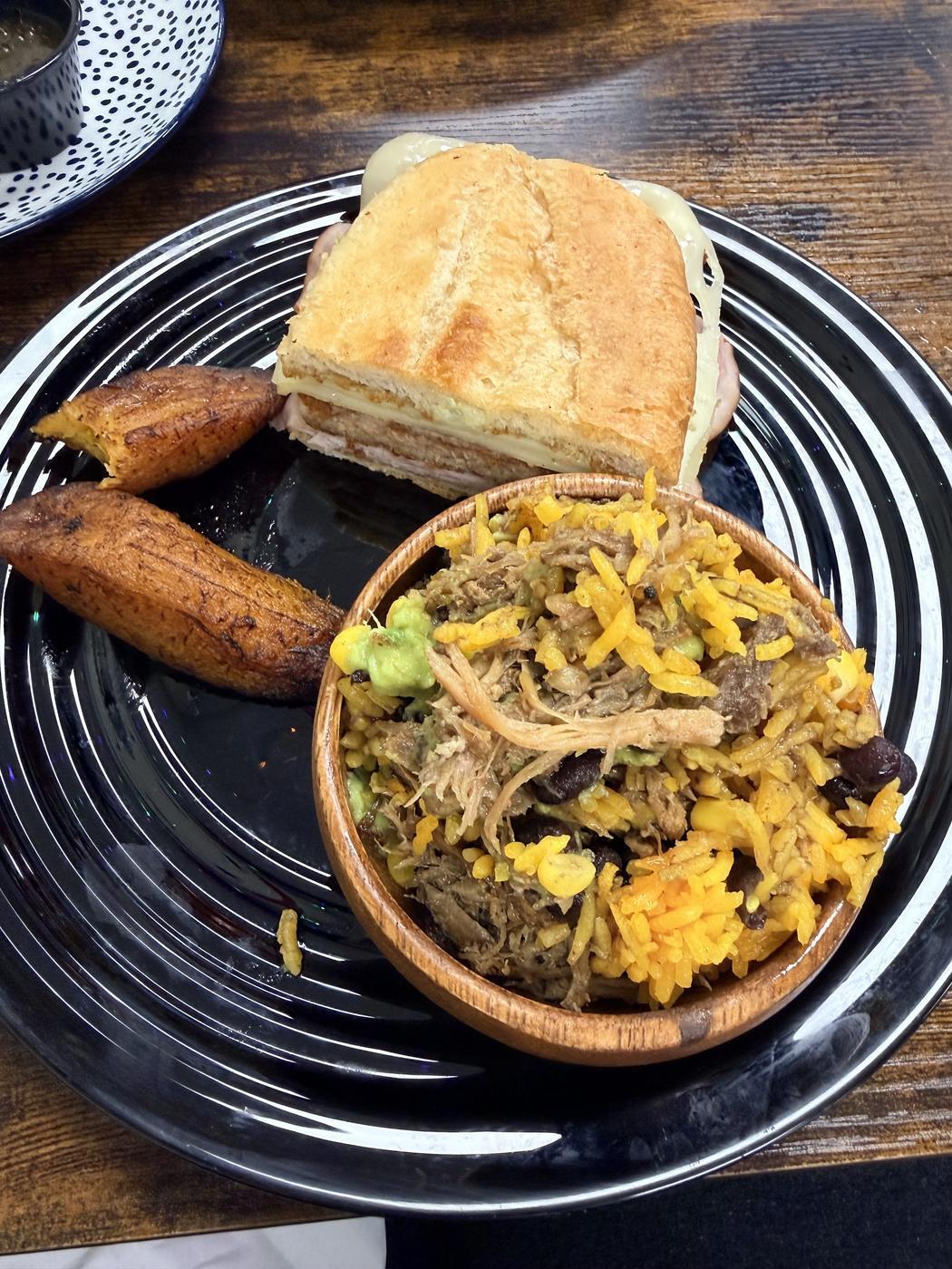 A pressed Cuban sandwich served with sweet plantains and a bowl of yellow rice